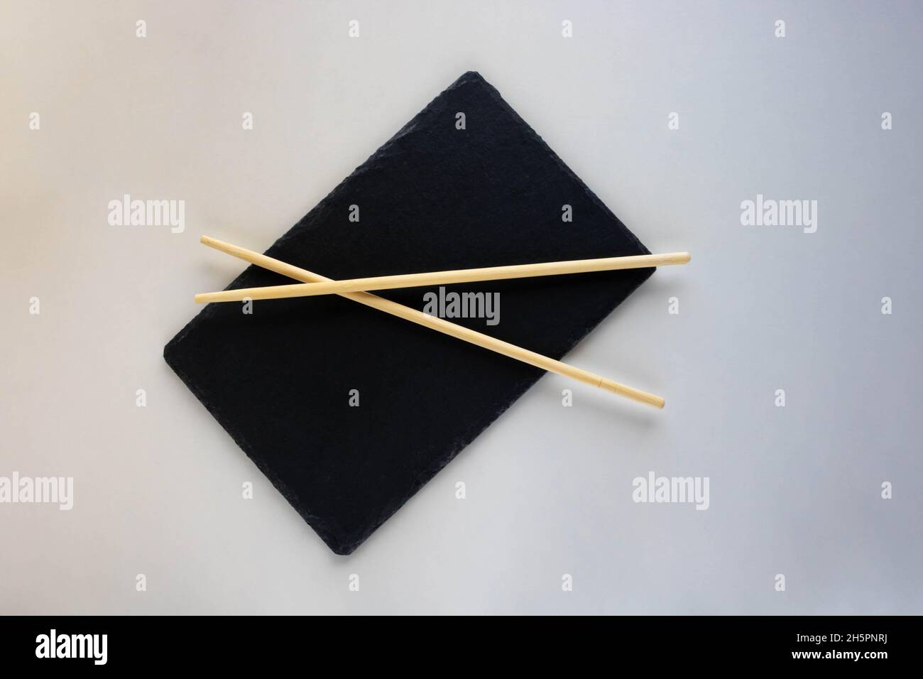 Asian cuisine is a Black Slate plate with chopsticks. An empty sushi plate on a white table. Stock Photo