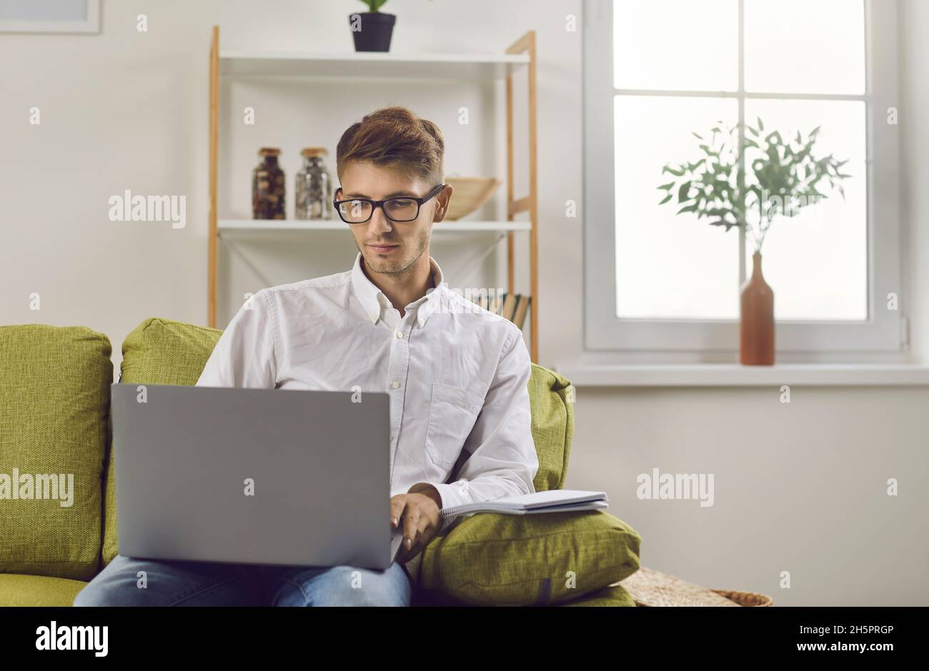 Young remote student using his laptop computer while sitting on couch ...