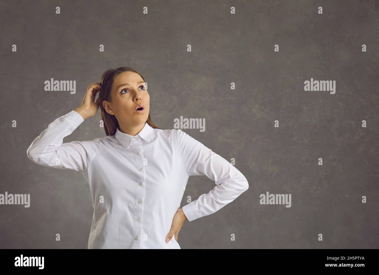 Young surprised woman scratching head looking up standing over studio background Stock Photo