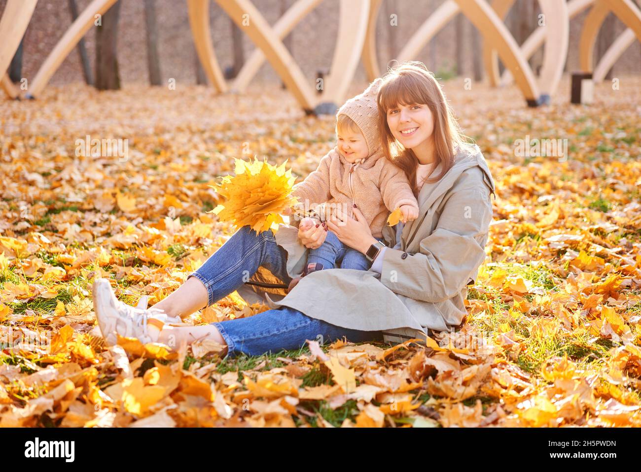 Portraits of a cute 1 year old baby girl and her young mother. Walking in Yellow Autumn Park. Leaf fall and yellow leaves. sunny day. Stock Photo