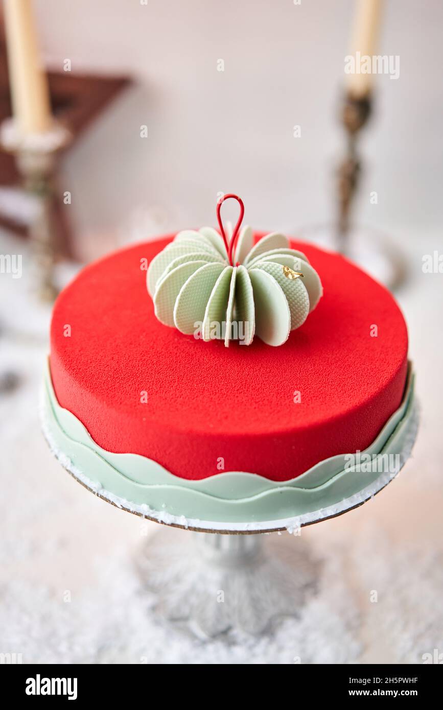 Mousse cake covered with red velour. Dessert on a snow-covered table. Modern european cake. French cuisine. Christmas theme Stock Photo