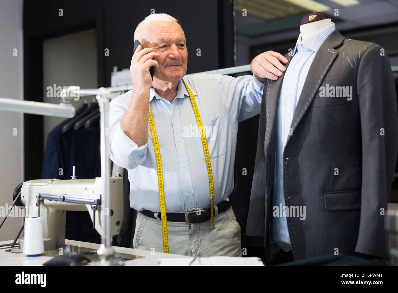 Professional tailor communicates with the client on mobile phone and takes notes in notebook Stock Photo