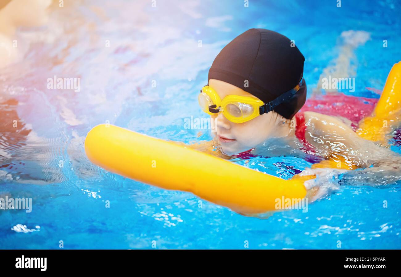 Little kid girl with glasses learning to swim with pool noodle Stock