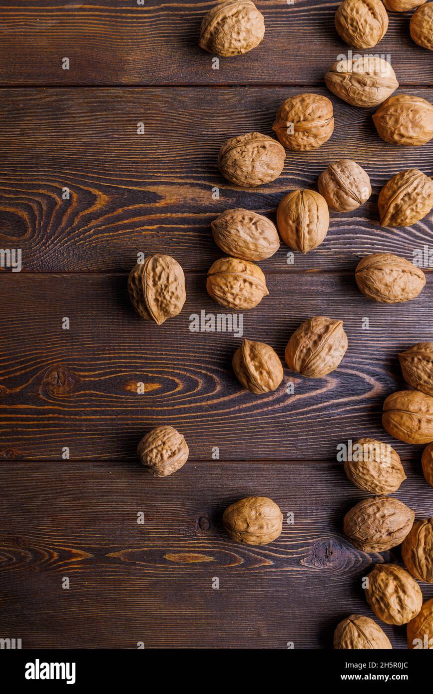 many walnuts with shells randomly scattered on brown wooden surface Stock Photo
