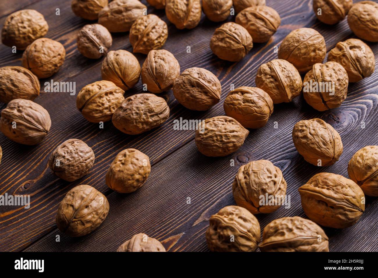 many walnuts with shells randomly scattered on brown wooden surface Stock Photo