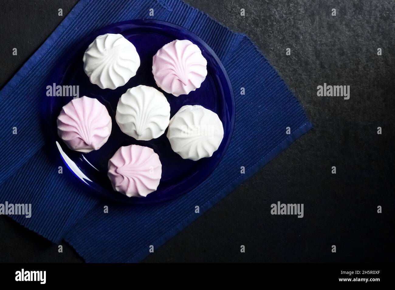 White and pink marshmallow on blue plate on black background. Flat lay, top view, copy space Stock Photo