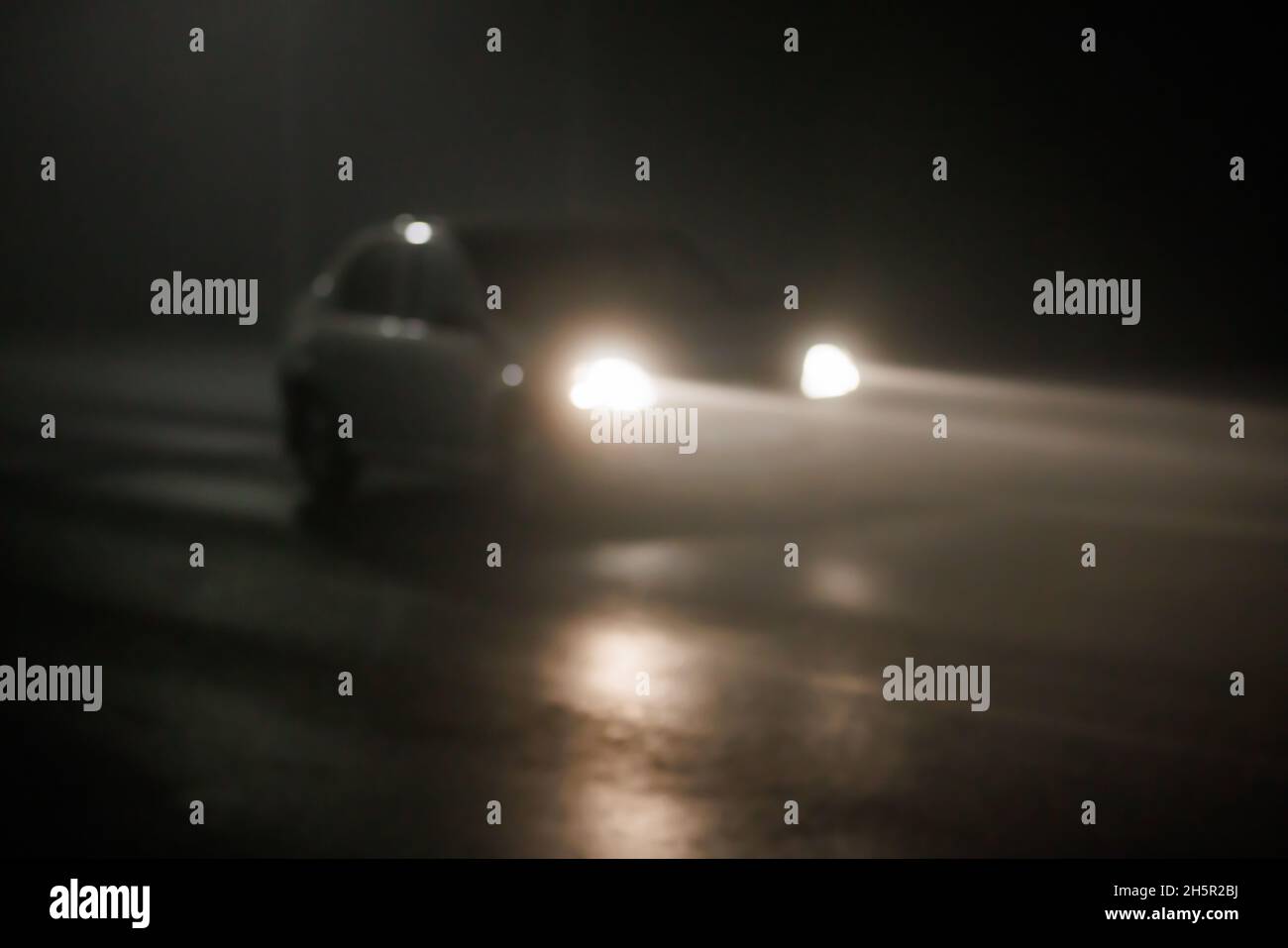 defocused photo of blurred car moving on empty night foggy road with long light beams out of headlights Stock Photo