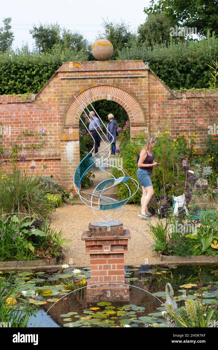 East Ruston Old Vicarage Gardens, near Stalham, Norfolk, UK. Visitors looking around walled area with lily pond,  pedestal mounted modern sculpture Stock Photo