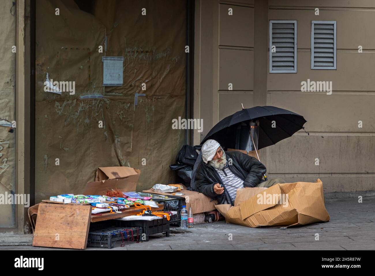 Istanbul, Turkey-Nov.9, 2021:Homeless man sitting on the street, near the wall and cart with his stuff near Sirkeci train Station in Istanbul.Number o Stock Photo