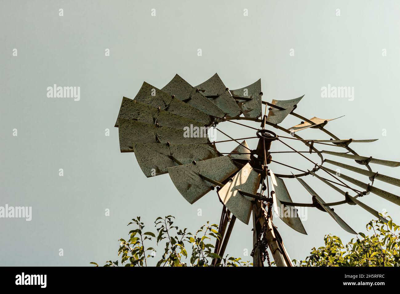 Vintage windmill against backdrop of grey sky and surrounded by green plants at base. Ontario, Canada. Stock Photo