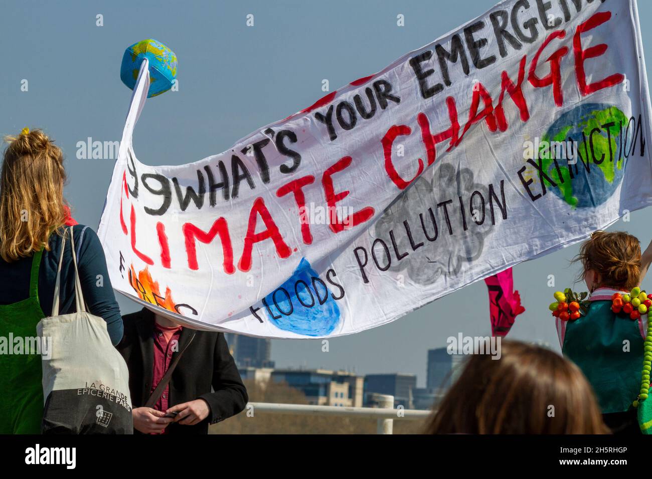 Street photograph of a group of climate change demonstrators with large homemade banner with backs to the camera.  Some buildings can be seen behind. Stock Photo