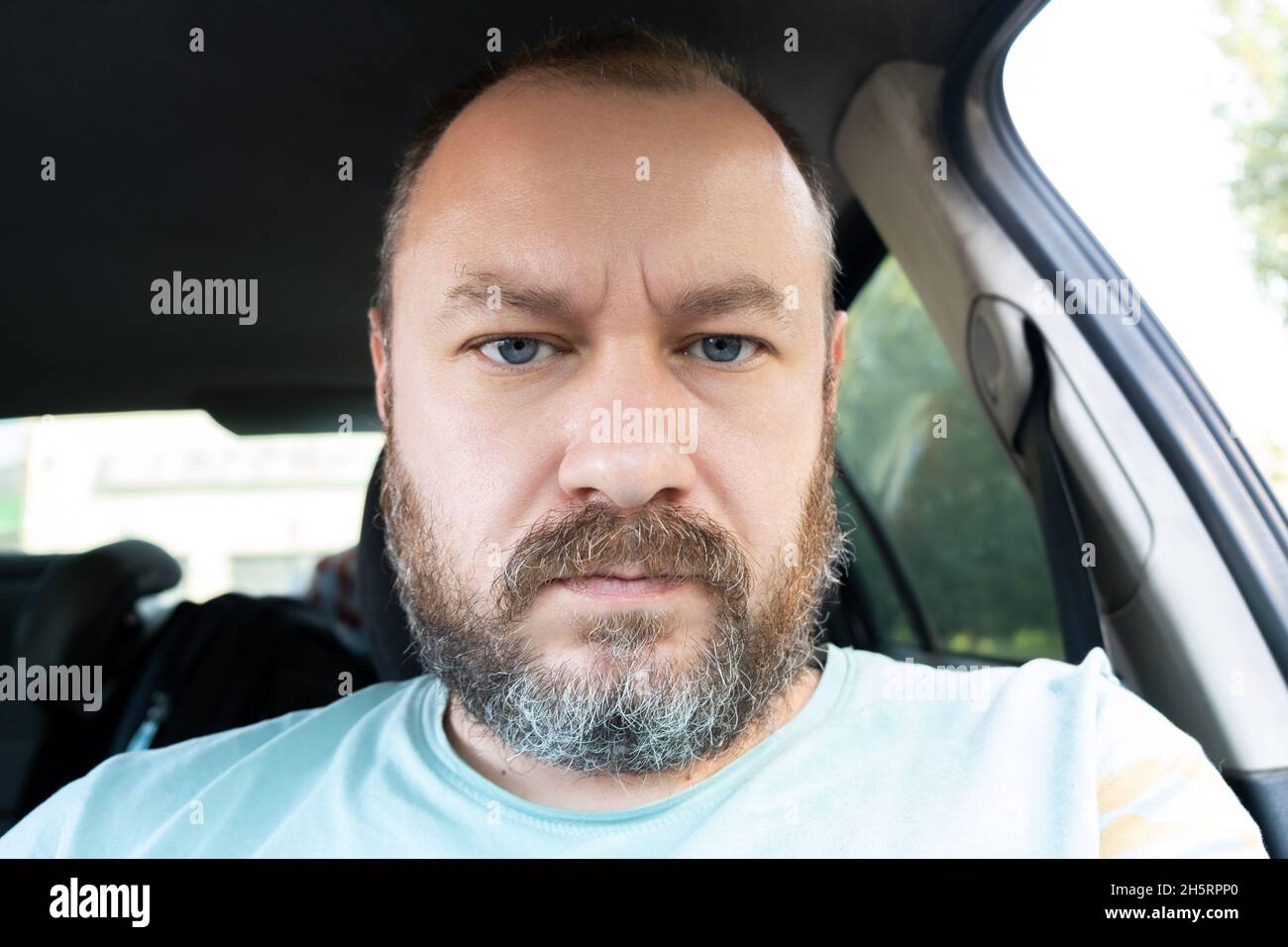 Portrait of an unshaven man 40 years old in a car. An ordinary man frowns at the camera. Stock Photo