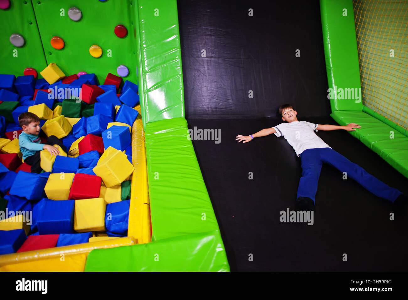 Two brothers lying on pool with colored foam cubes and trampoline in