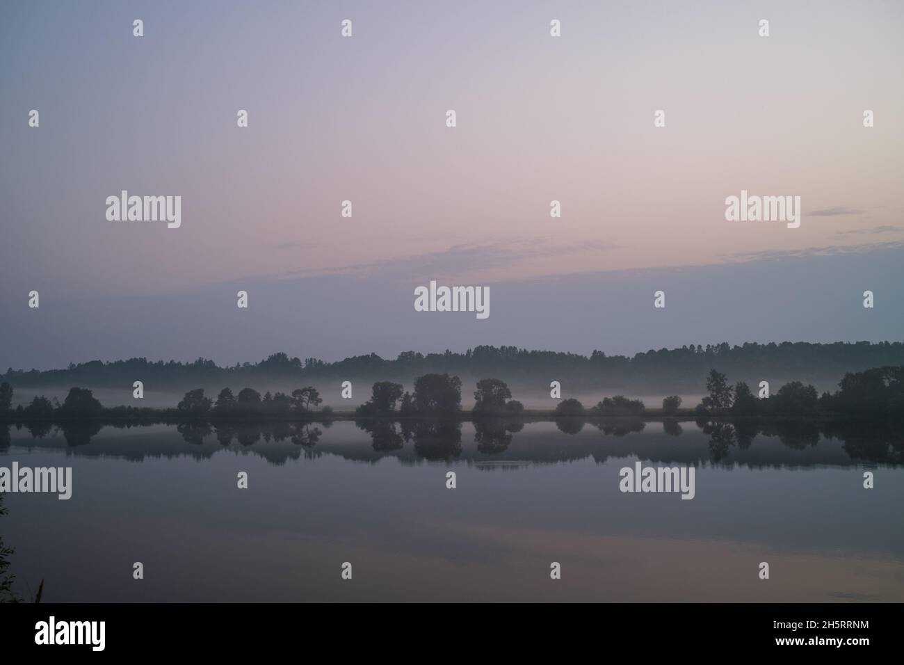 misty morning by the lake with calm water, fog and reflections of trees ...