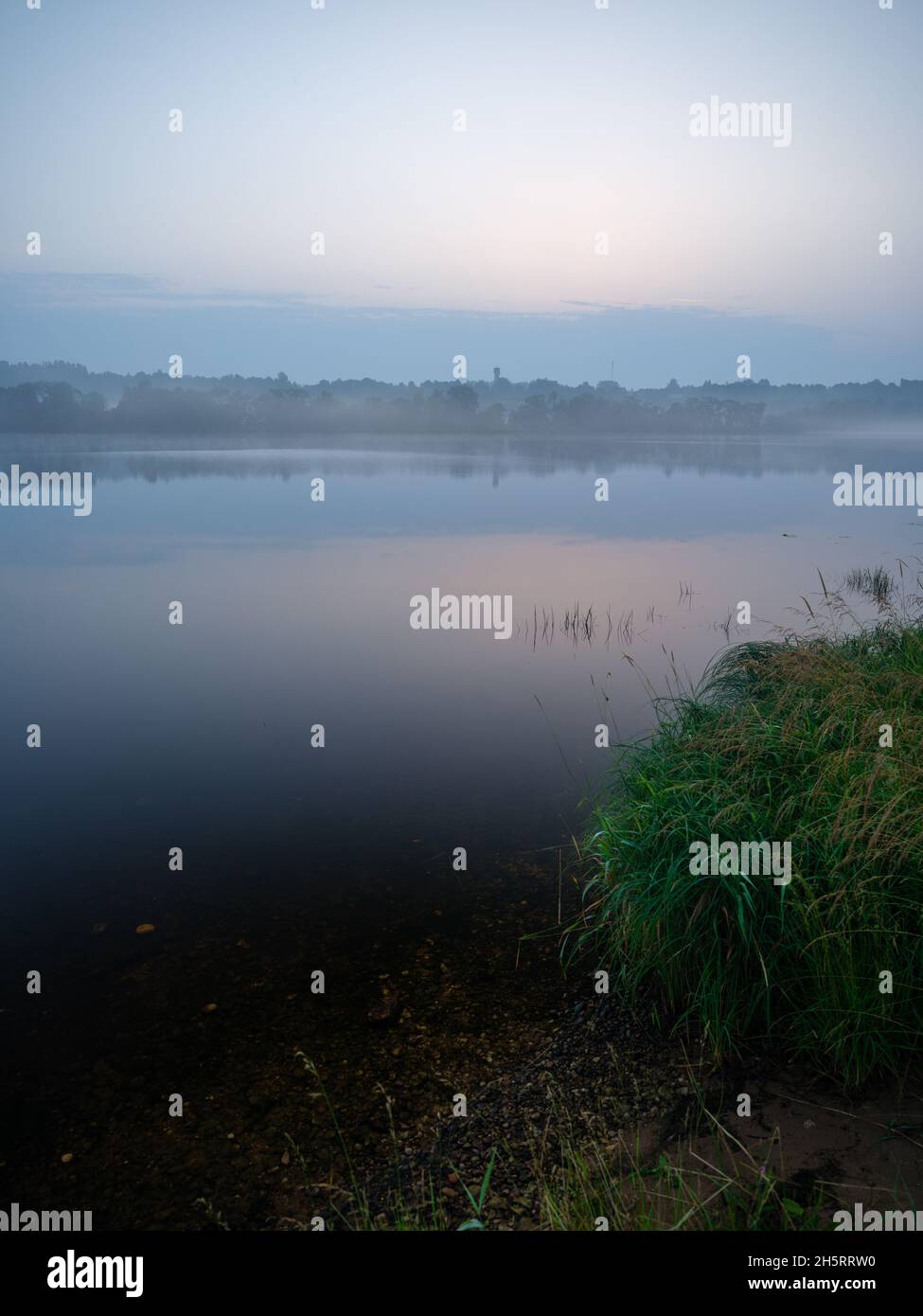 misty morning by the lake with calm water, fog and reflections of trees ...