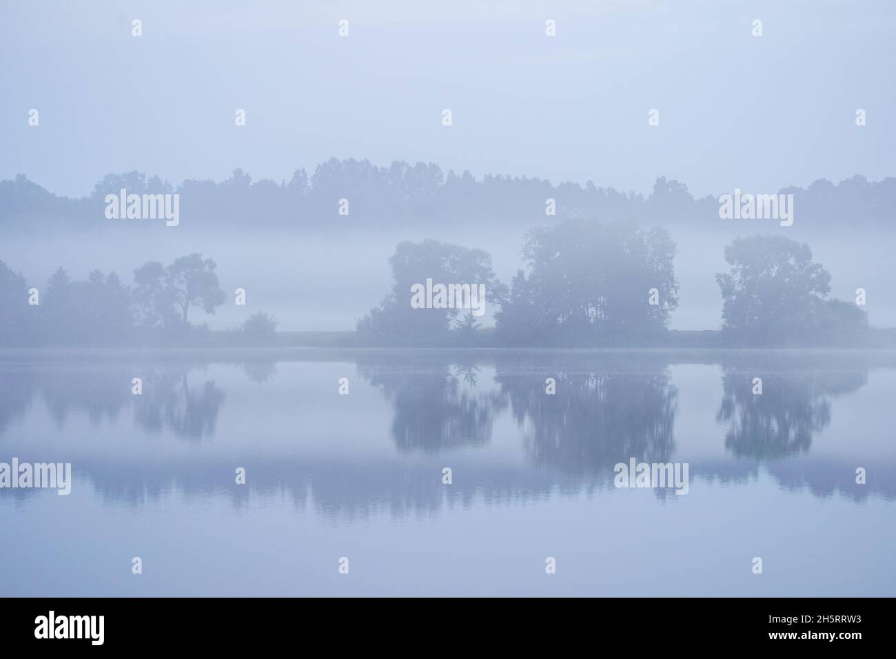 misty morning by the lake with calm water, fog and reflections of trees ...