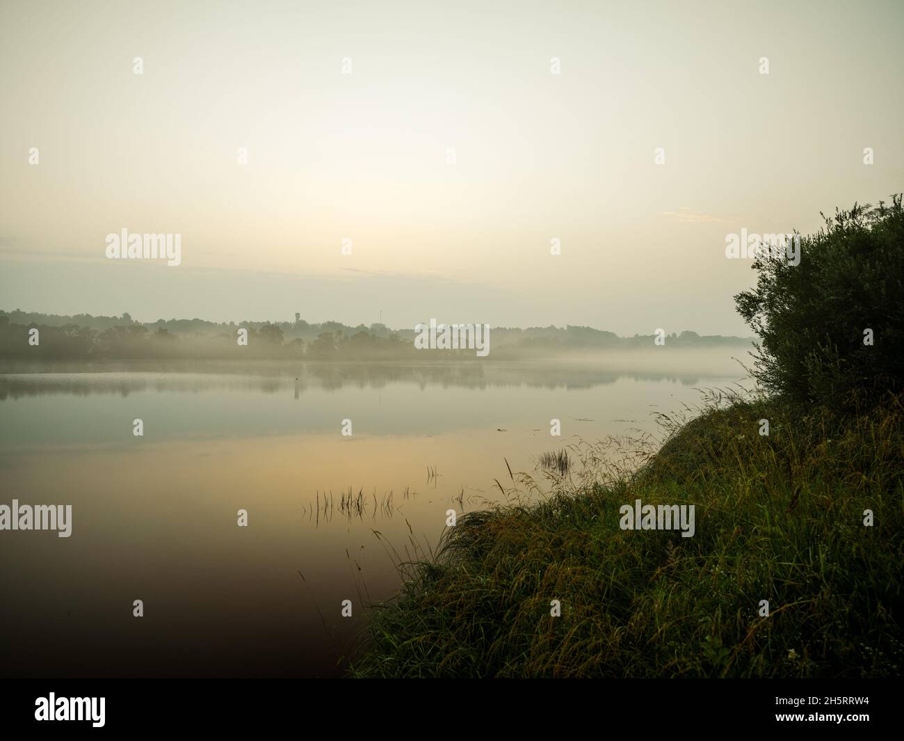 misty morning by the lake with calm water, fog and reflections of trees ...
