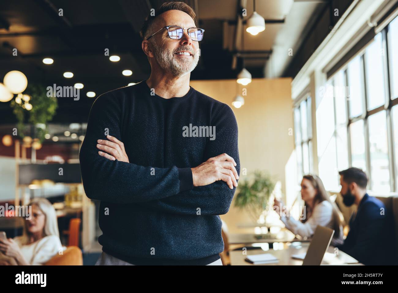 Contemplative businessman standing in a co-working space. Happy mature businessman smiling while thinking of new business ideas. Experienced entrepren Stock Photo
