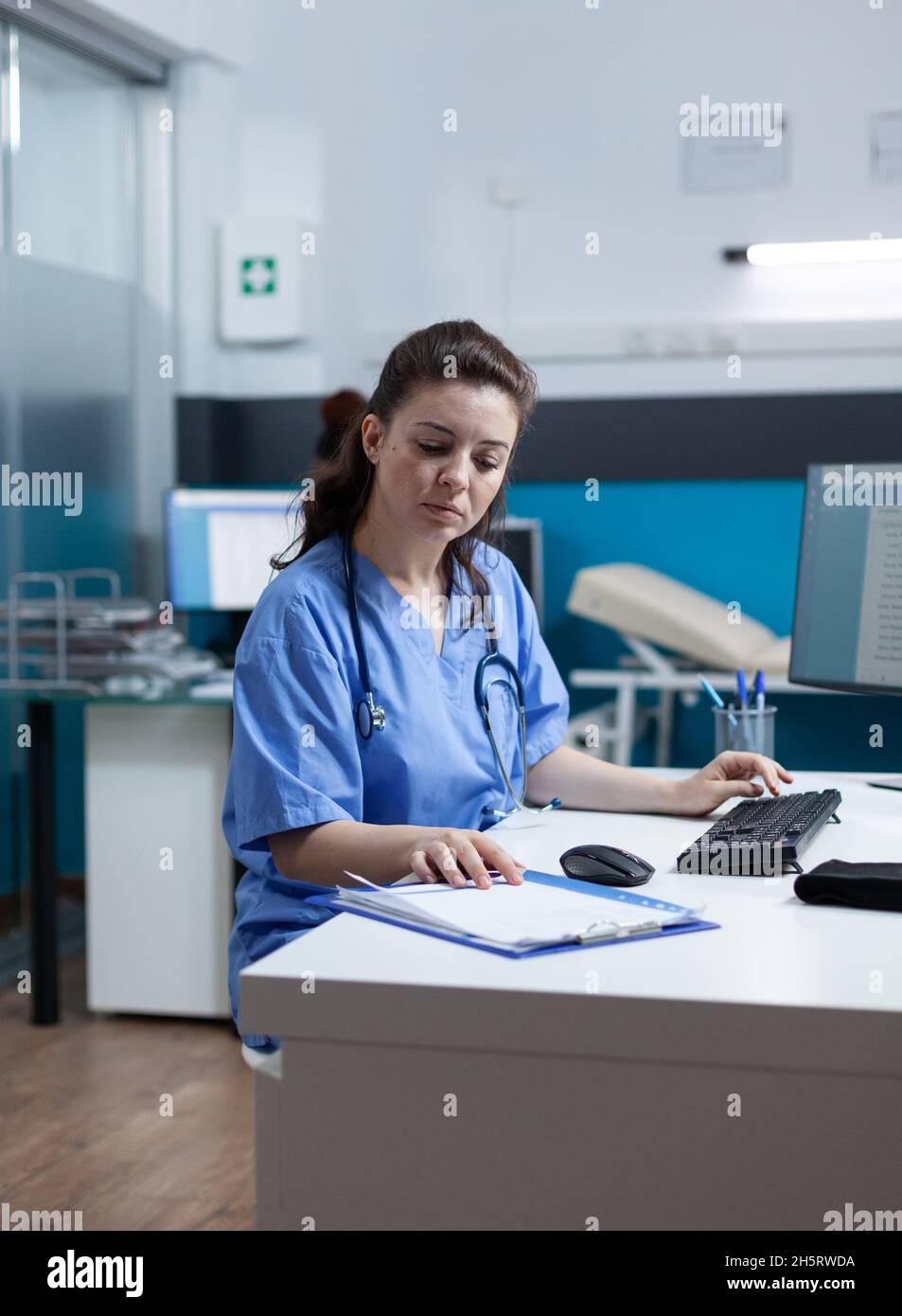 Practitioner nurse with stethoscope analyzing healthcare treatment on medical paperwork typing sickness expertise working in hospital examination office. Woman asisstance checking disease results Stock Photo