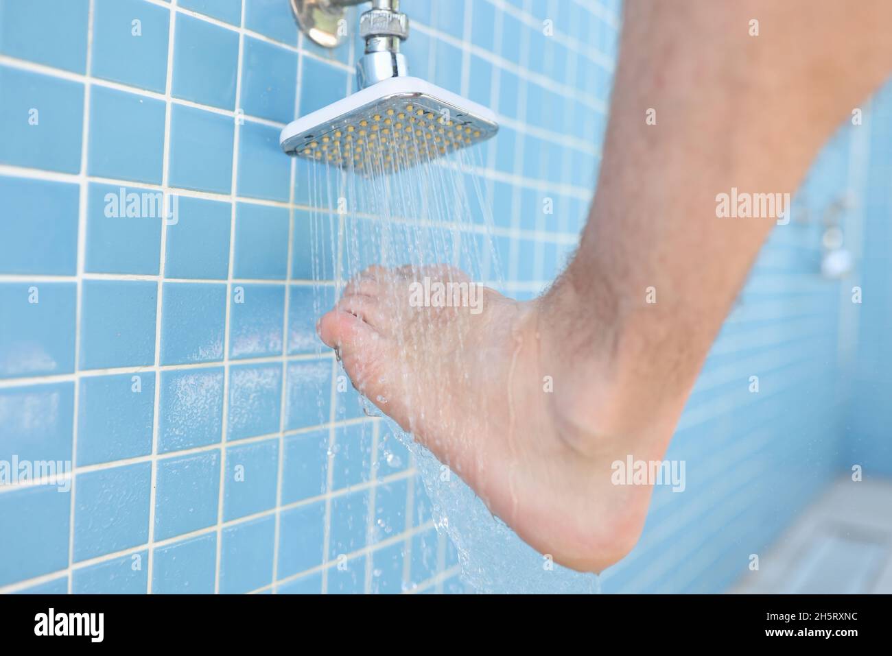 Man washing his feet from sand under shower on beach closeup. Foot