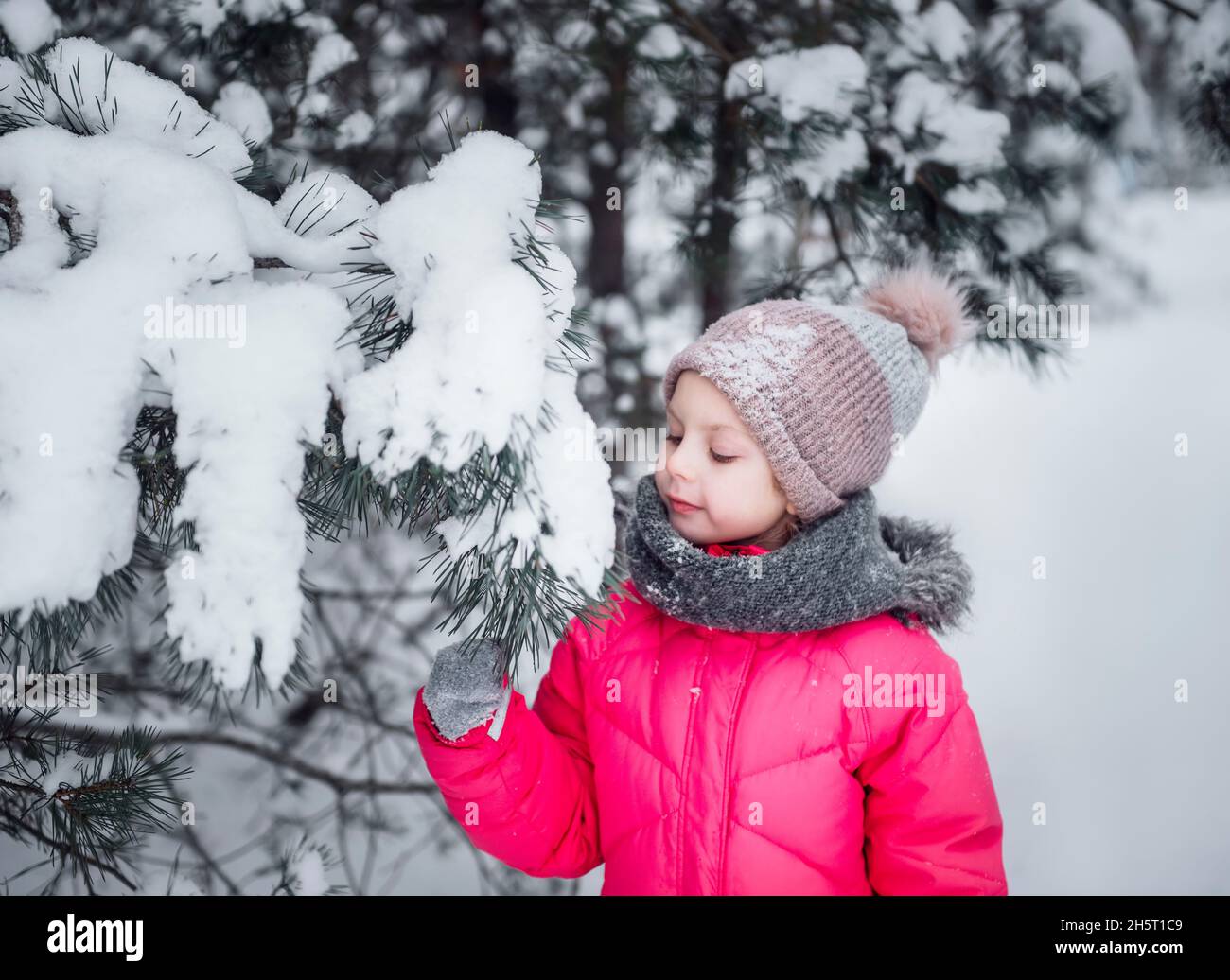 A little girl in a bright jacket plays in the winter snowy forest Stock ...