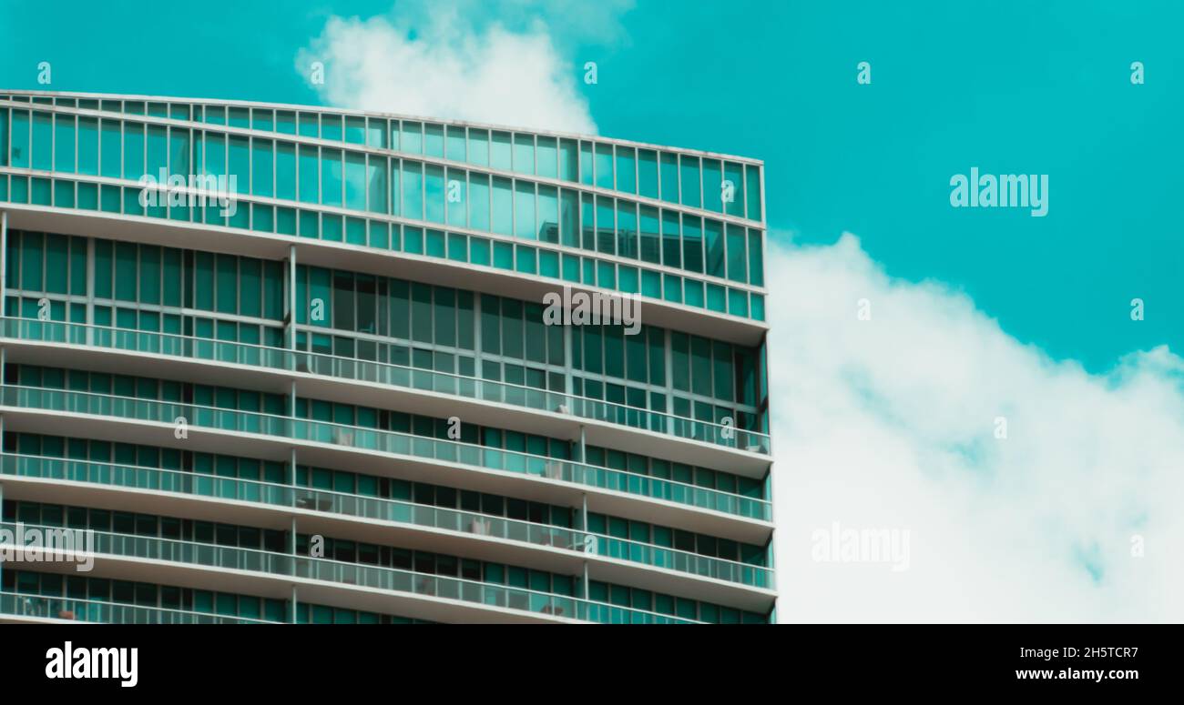 Modern highrise glass building under a blue sky with fluffy clouds ...