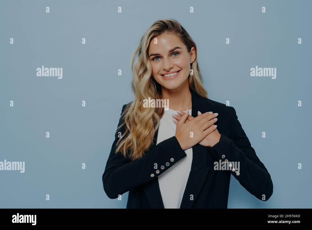 Cheerful blonde girl showing her appreciation and gratitude by placing hands on chest Stock Photo