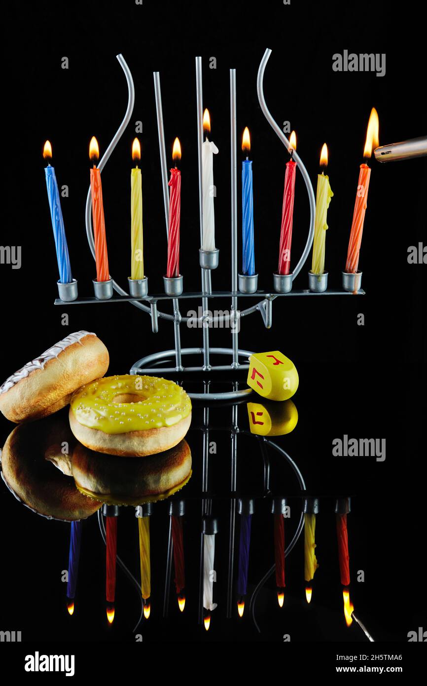 Happy Hanukkah and Hanukkah Sameach - traditional Jewish candlestick with burning candles and donuts against black background with reflection. Stock Photo
