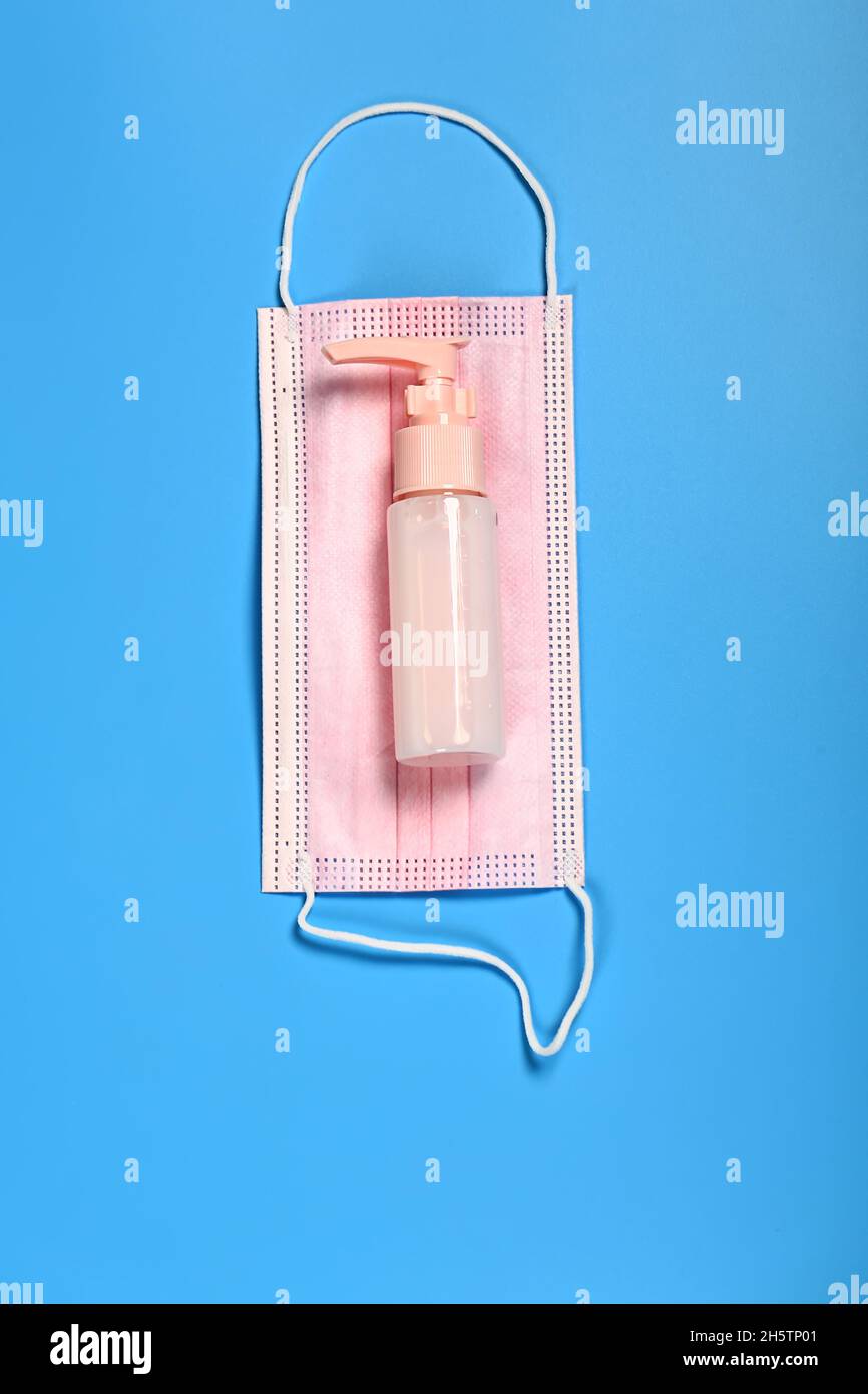 pink medical mask and sanitizer on blue background Stock Photo