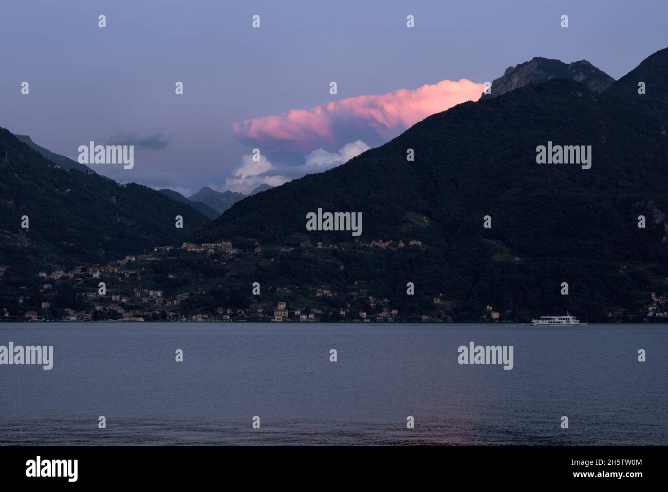 View of Bellano, a ferry and a pink cloud at Lake Como at blue hour, Italy Stock Photo