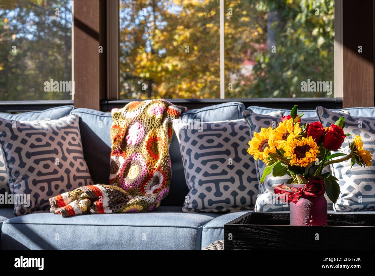 Cozy patio corner in a screened porch with flower bouquet in a vase, autumn leaves and woods in the background. Stock Photo