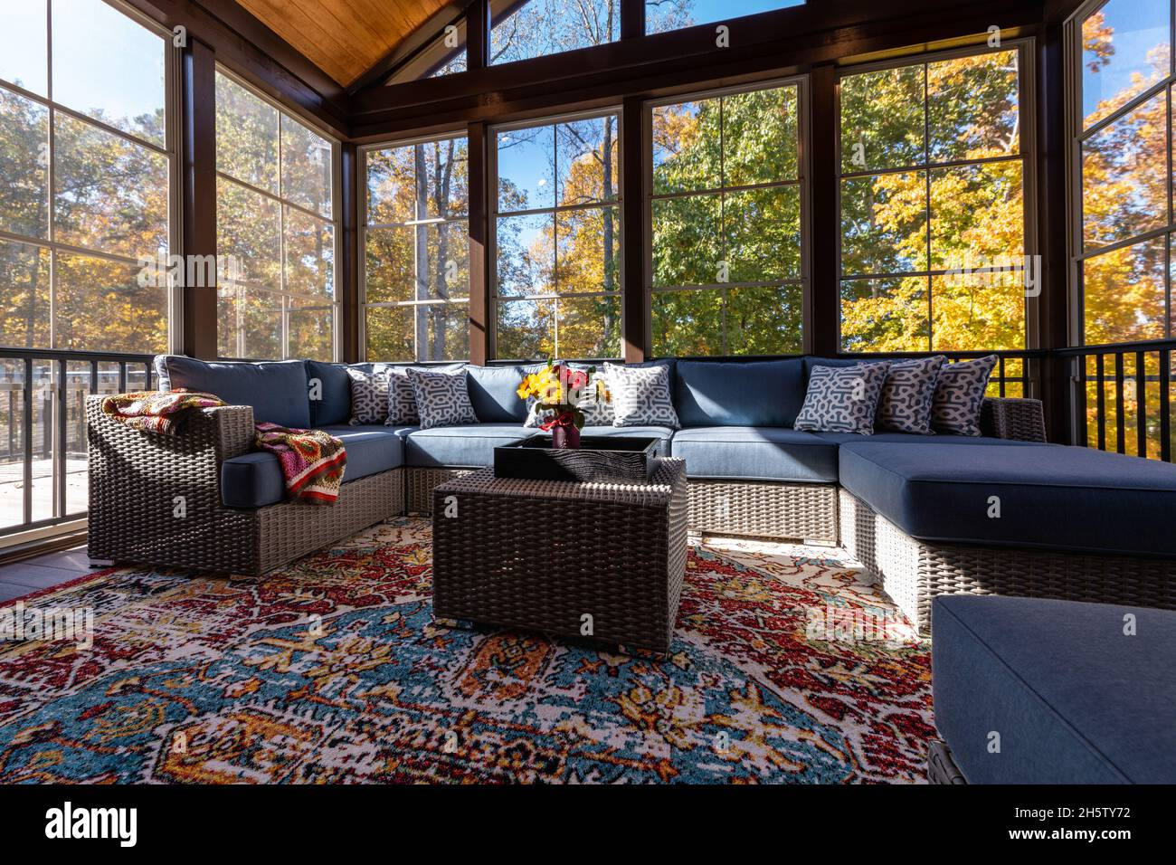 Cozy screened porch with contemporary furniture and flower bouquet in a vase, autumn leaves and woods in the background. Stock Photo