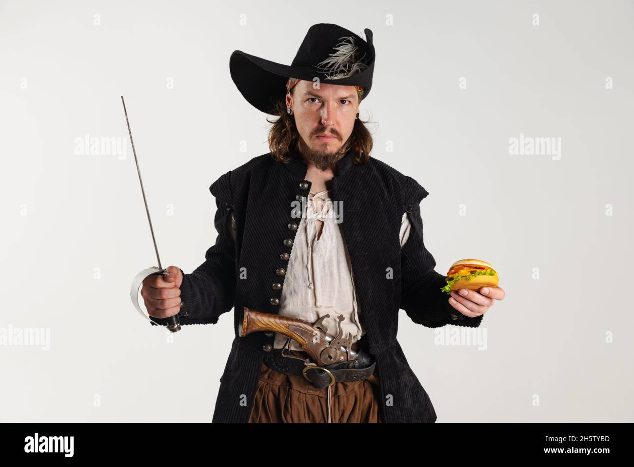 Cropped portrait of brutal man, pirate in vintage costume with sword holding burger isolated over white background Stock Photo