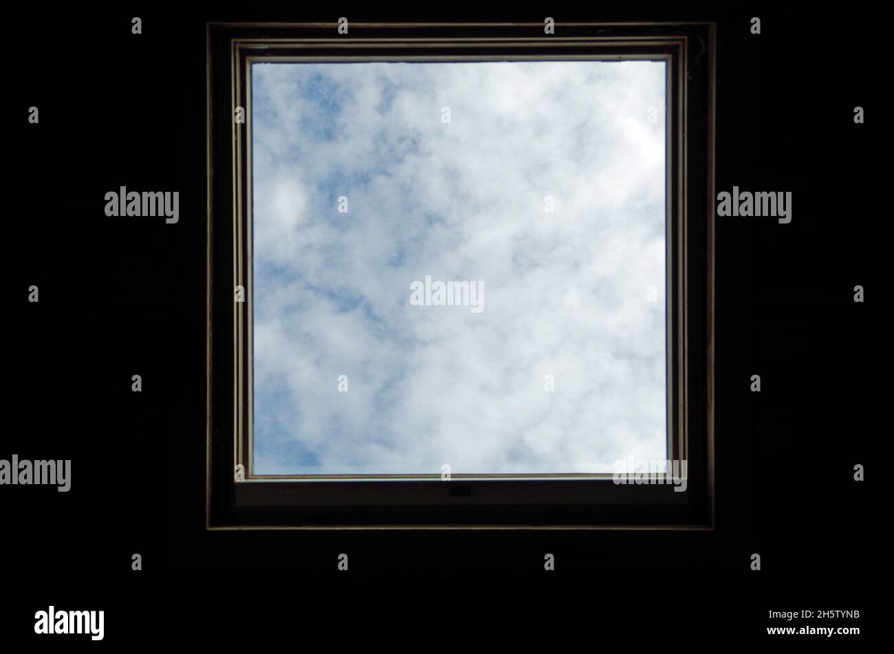 Skylight surrounded by darkness. Blue sky and clouds. Conceptual metaphor. Stock Photo