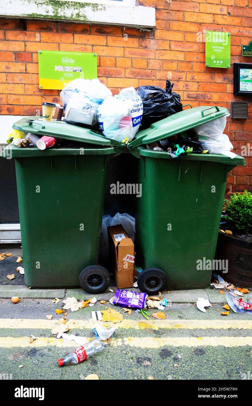 Two green household recycling bins outside holiday cottages overfilled