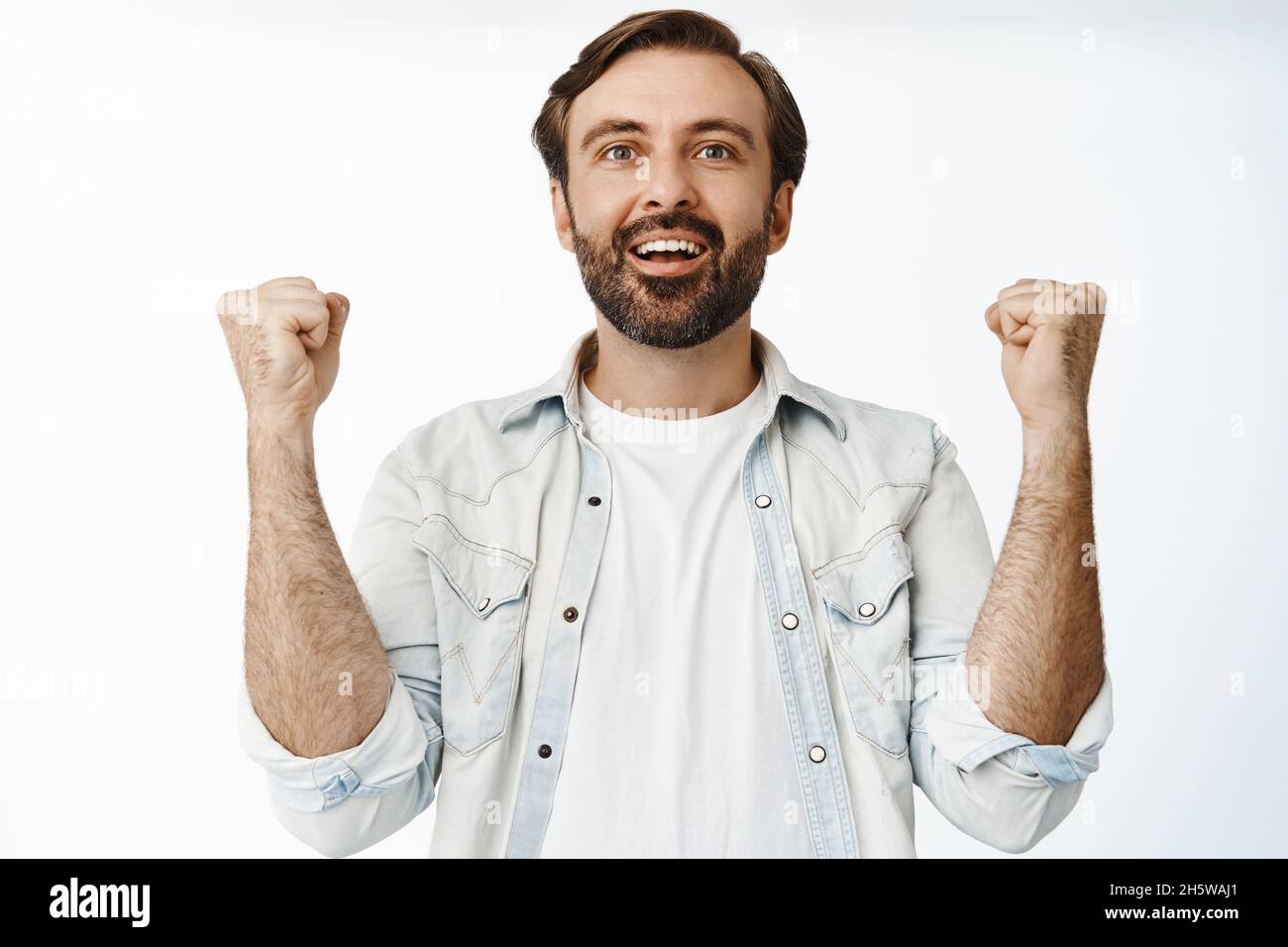 Happy pleased guy fist pmps, looking at smth with relieved joyful face, smiling pleased, watching sport game, standing over white background Stock Photo