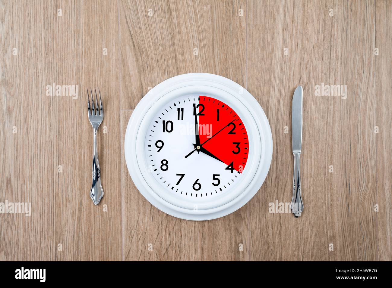 Clock with one portion marked in red. Concept of intermittent fasting, a diet that provides benefits such as the regenerative mechanism of autophagy. Stock Photo