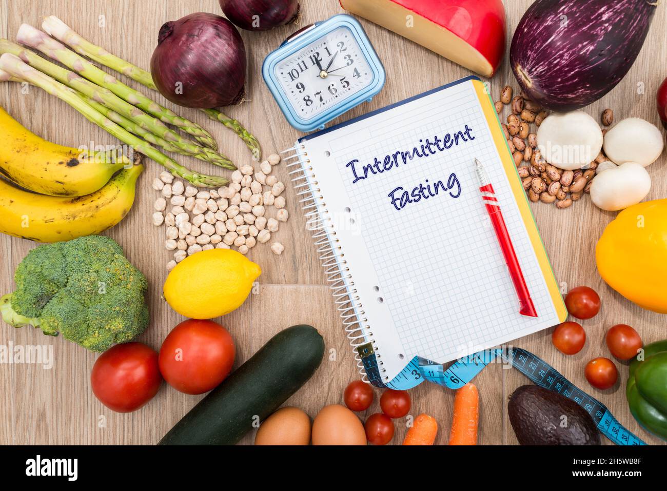 Healthy food around a notebook and a clock with a wooden background. Conceptual image of intermittent fasting, a diet with benefits such as the regene Stock Photo