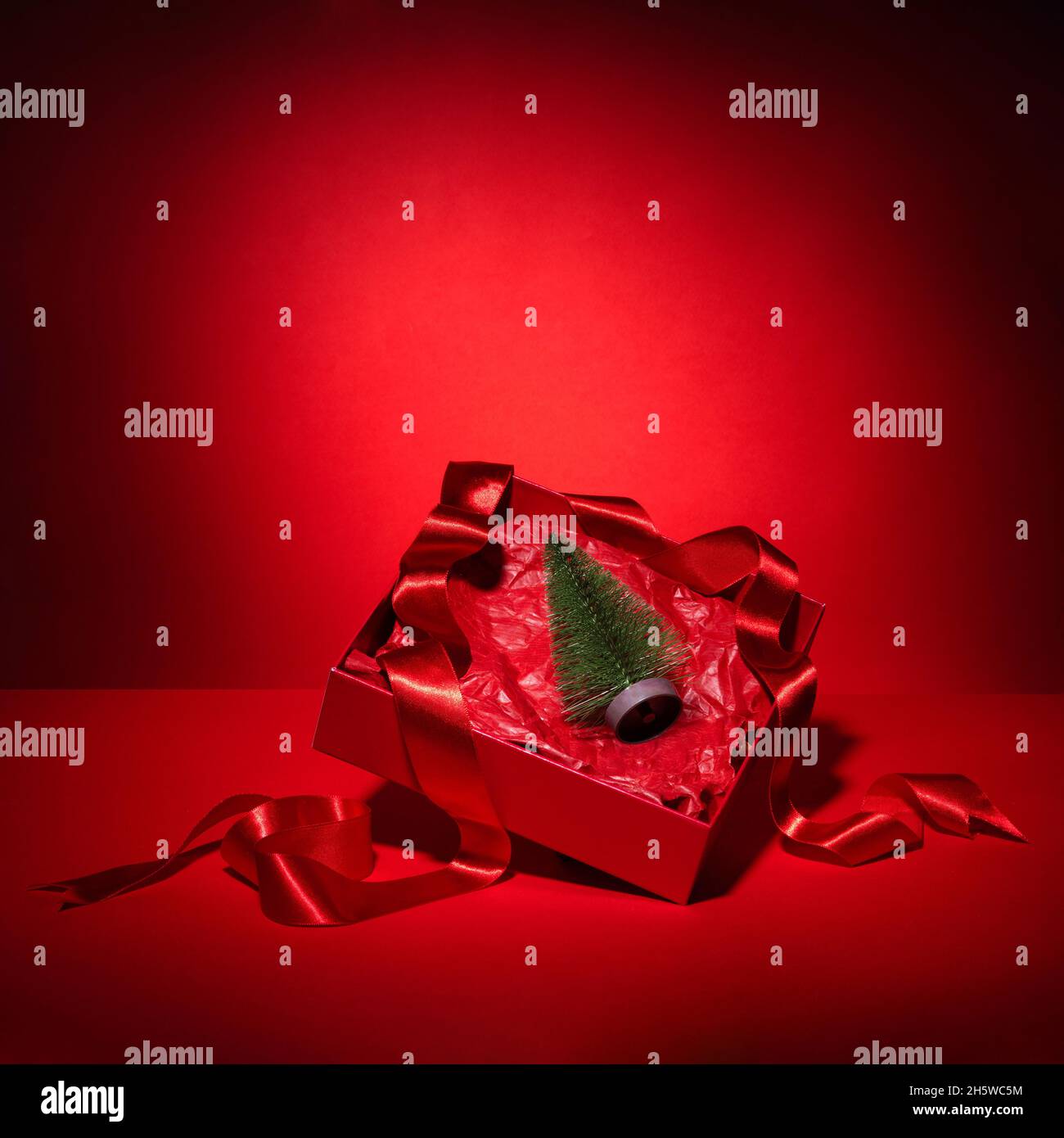 Red festive gift box with ribbon and Christmas tree. Conceptual composition. Red monochrome Minimalism Copy space Stock Photo