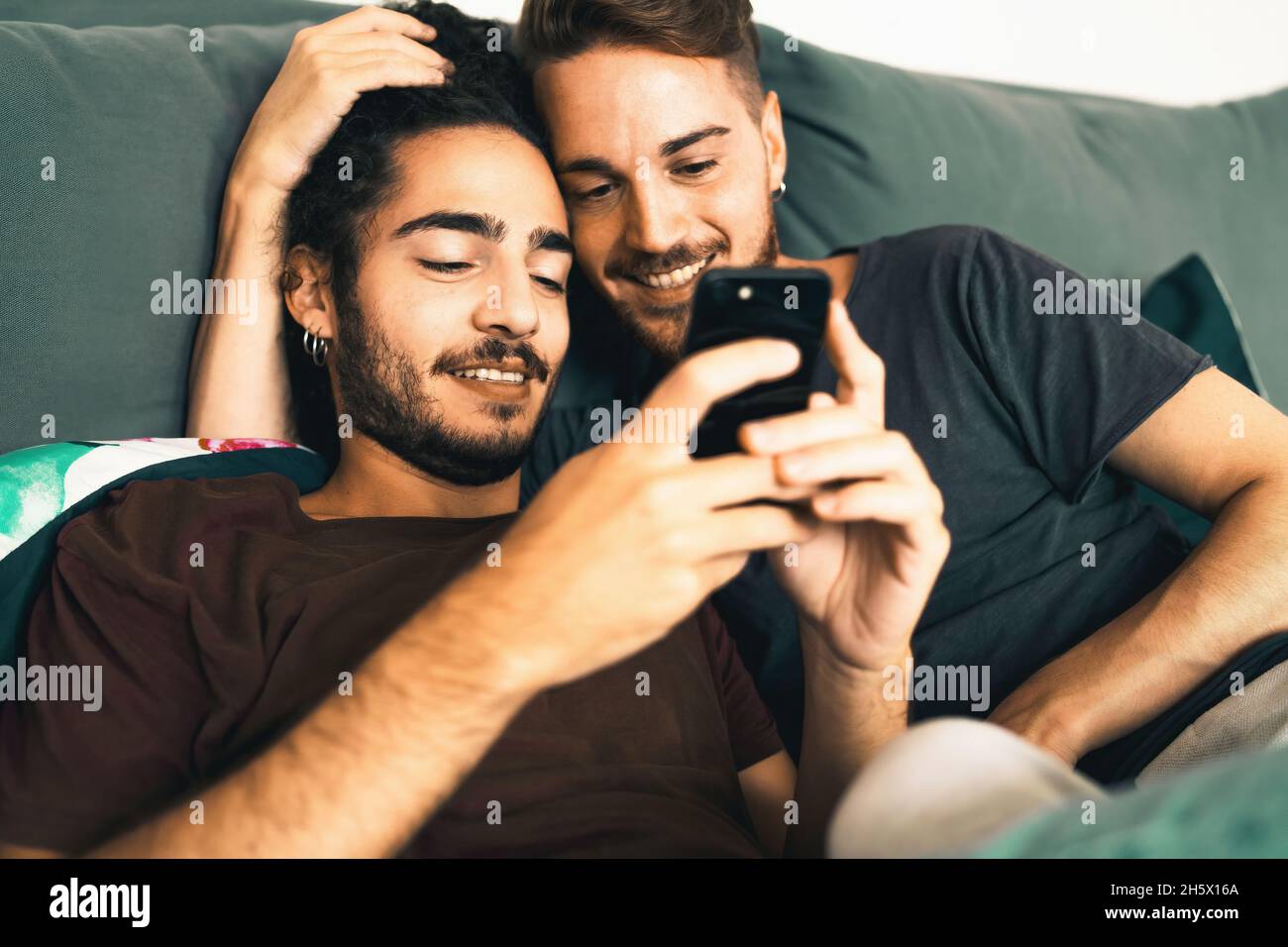 Male gay couple using smartphone in the bedroom - homosexual LGBT concept - focus on the left man Stock Photo