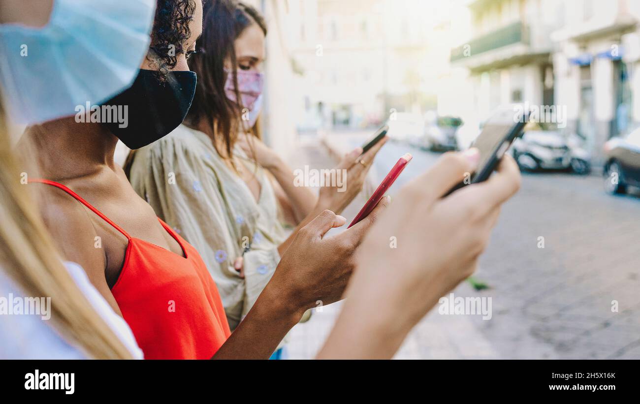 Group of friends using smartphone and the internet outdoors with face mask - concept of young people using tech and social networks together during co Stock Photo