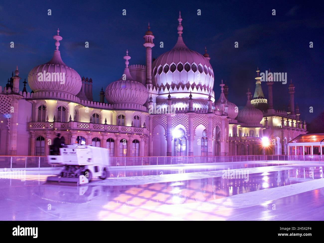 The Royal Pavilion, Brighton, lit up with coloured LED uplighters behind the winter ice skating rink erected in the Pavilion gardens. Brighton, East Sussex, England, UK. Preparing the surface of the ce rink for another skating session. Stock Photo