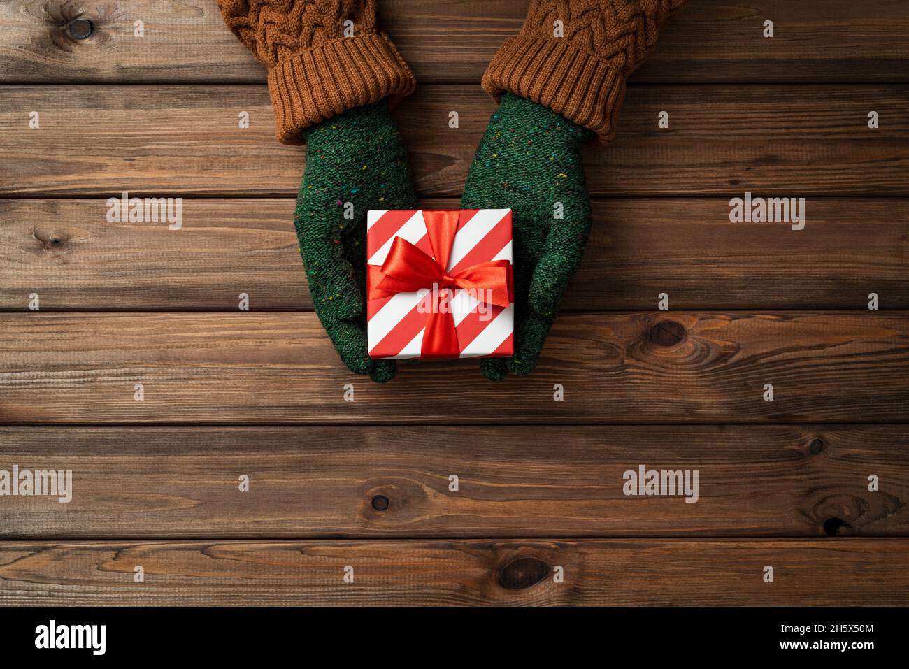 Christmas card with gift in the hands of a girl on wooden background with copy space for text Stock Photo