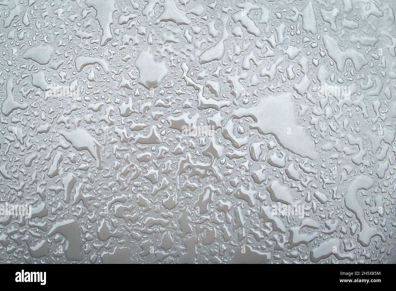 Irregular patterned water drops on a silver-coloured shiny metal surface Stock Photo