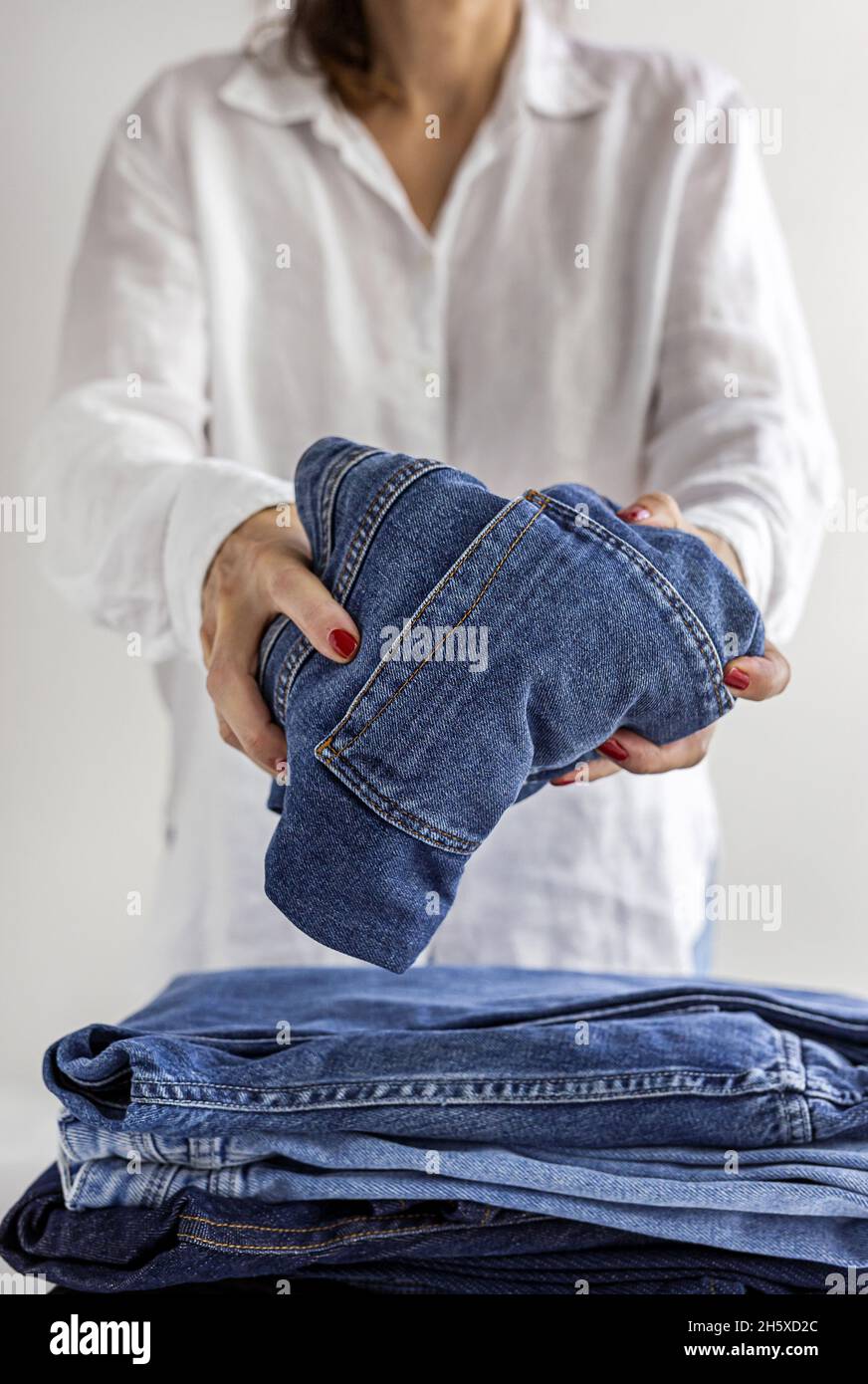 Crop anonymous female in white shirt with stack of blue jeans in hands ...