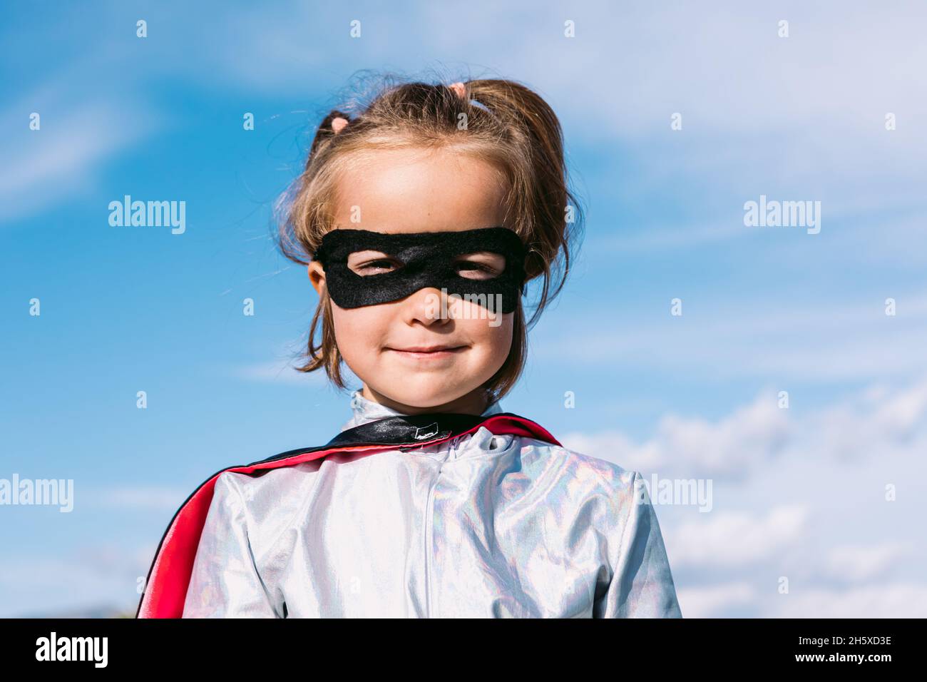 Cute kid wearing masquerade superhero costume and eye mask standing
