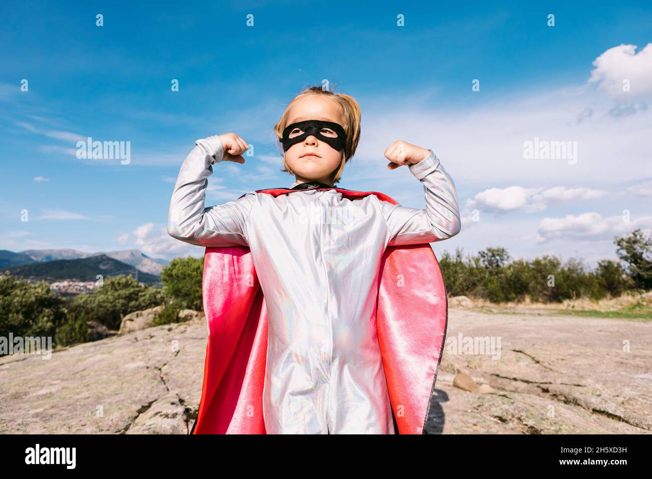 Strong girl in superhero cape raising hands for showing strength for