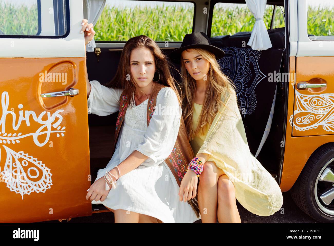 Two pretty girls dressed in summer clothes sitting on the floor of the van looking at the camera Stock Photo