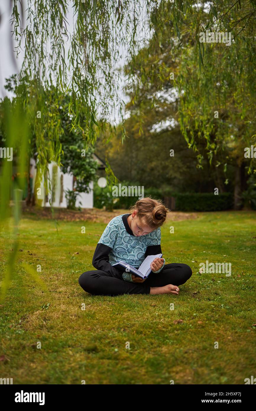 Full body of concentrated barefoot girl reading interesting book while ...