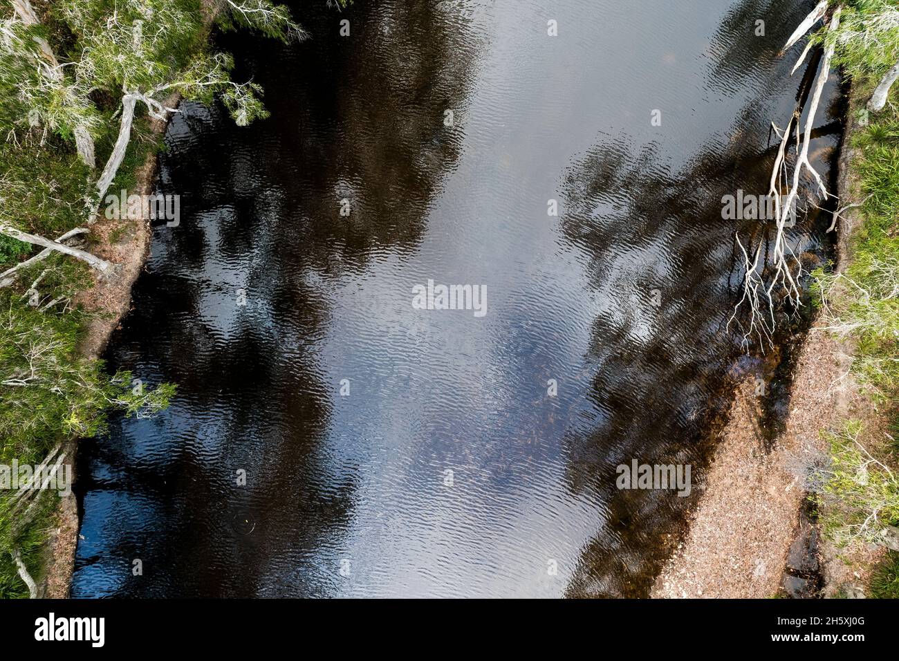 A low aerial of the ripples in the shallow water of a tree lined ...